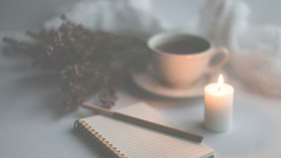 Libreta, taza de infusión y vela encendida sobre una mesa clara, para escribir afirmaciones para la salud