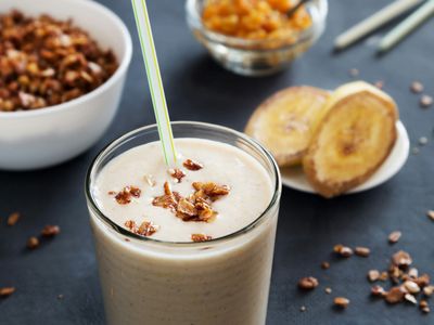 Vaso de batido cremoso de banano con granola por encima y banano en rodajas al lado