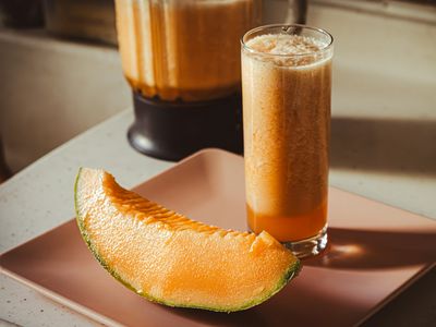 Vaso de batido anaranjado junto a una tajada de fruta de pulpa naranja