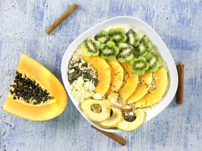 Bowl de yogur con papaya, kiwi, avena y semillas, junto a media papaya