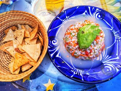 Ceviche de pescado con aguacate en un plato azul, con tostadas de maíz al lado