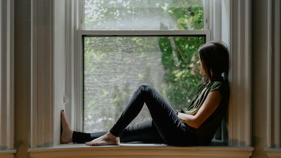 Mujer sentada en calma junto a una ventana, una pausa que ayuda a entender cómo bajar el cortisol
