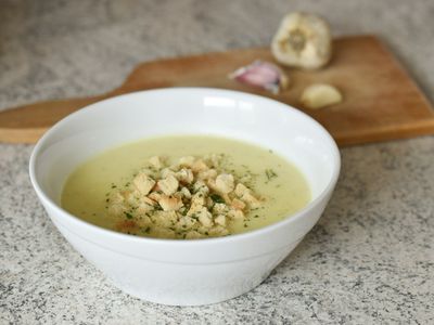 Tazón de crema blanca de coliflor con crutones y perejil, con ajos al fondo
