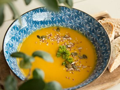 Crema de zapallo anaranjada con semillas tostadas en un bol azul, con pan al lado