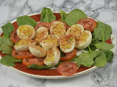 Huevos duros en mitades sobre rodajas de tomate y hojas de espinaca