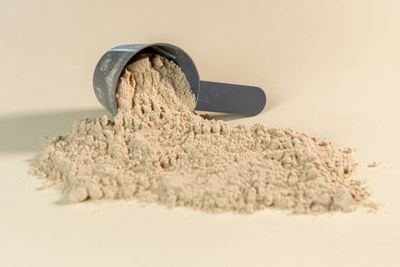Cuchara medidora con polvo de suplemento derramado sobre una mesa clara