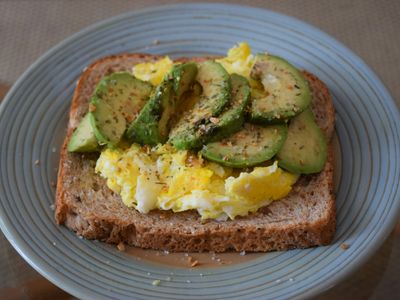 Tostada de pan integral con huevos revueltos y láminas de aguacate