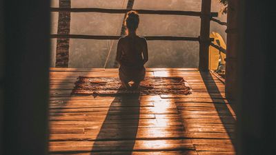 Persona meditando sentada en el piso frente a una ventana con luz cálida, una forma de practicar mantras