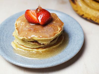 Pila de pancakes con una frutilla encima y miel cayendo