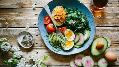 Plato con huevos duros, verduras y hojas verdes, junto a aguacate y huevos, para calcular cuánta proteína necesito al día