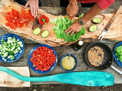 Manos picando verduras frescas sobre una mesa con varios platos saludables