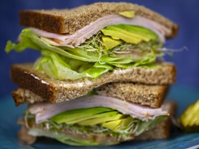 Sánduche de pan integral con aguacate, lechuga, brotes y fiambre de ave