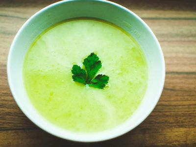 Tazón de sopa verde cremosa con una hoja de perejil