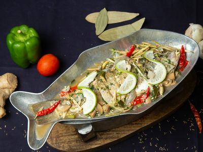 Pescado entero al vapor con rodajas de limón y ají en una fuente con forma de pez