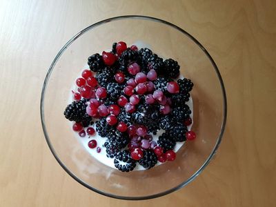 Bol de vidrio con yogur natural, moras y grosellas